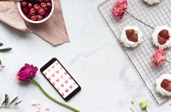Un cellulare con sfondo a cuori e una rosa accanto su una scrivania ben preparata, a simboleggiare le app e i siti d'incontro